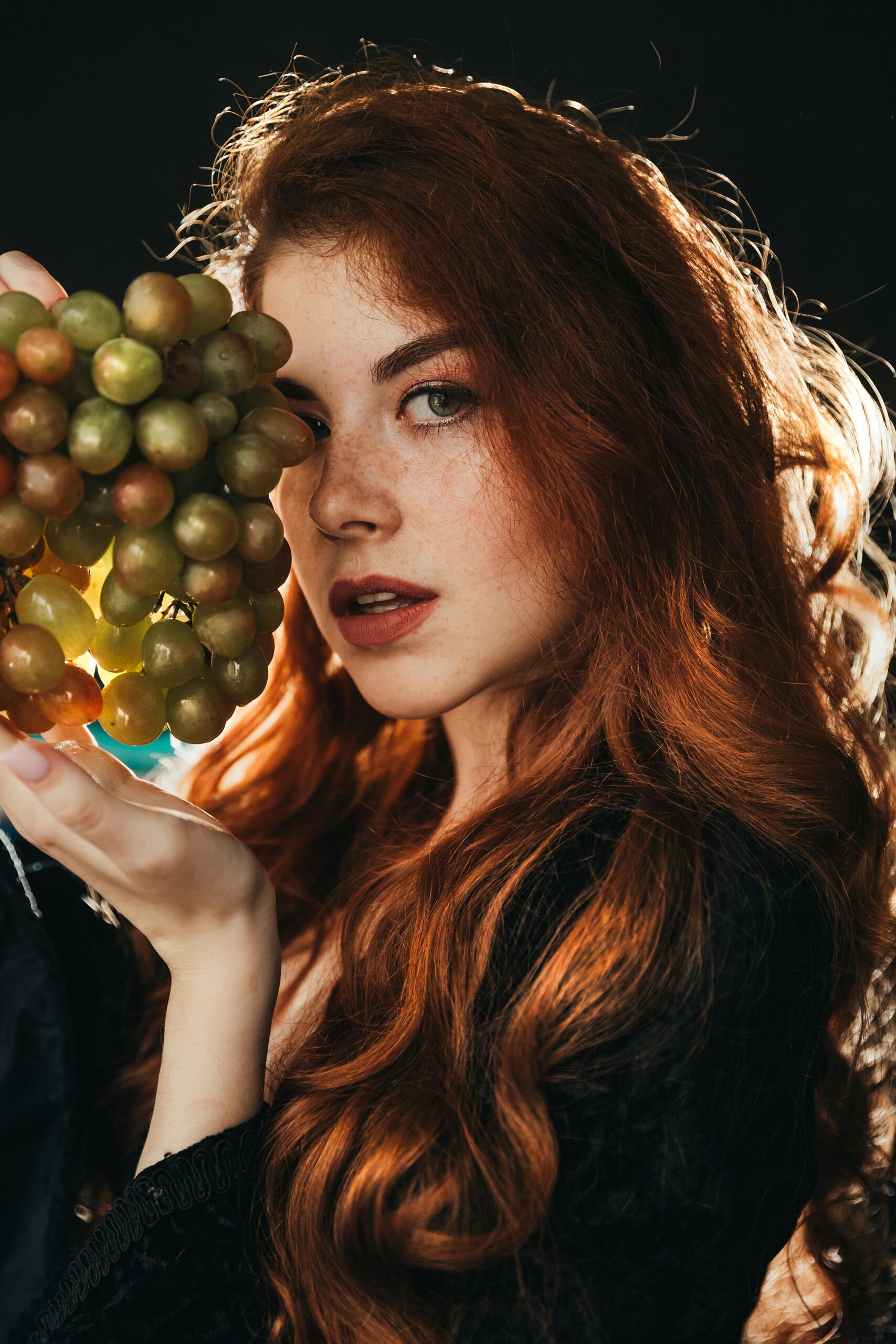 A beautiful red-haired woman elegantly holding a bunch of grapes, showcasing glamour and femininity.